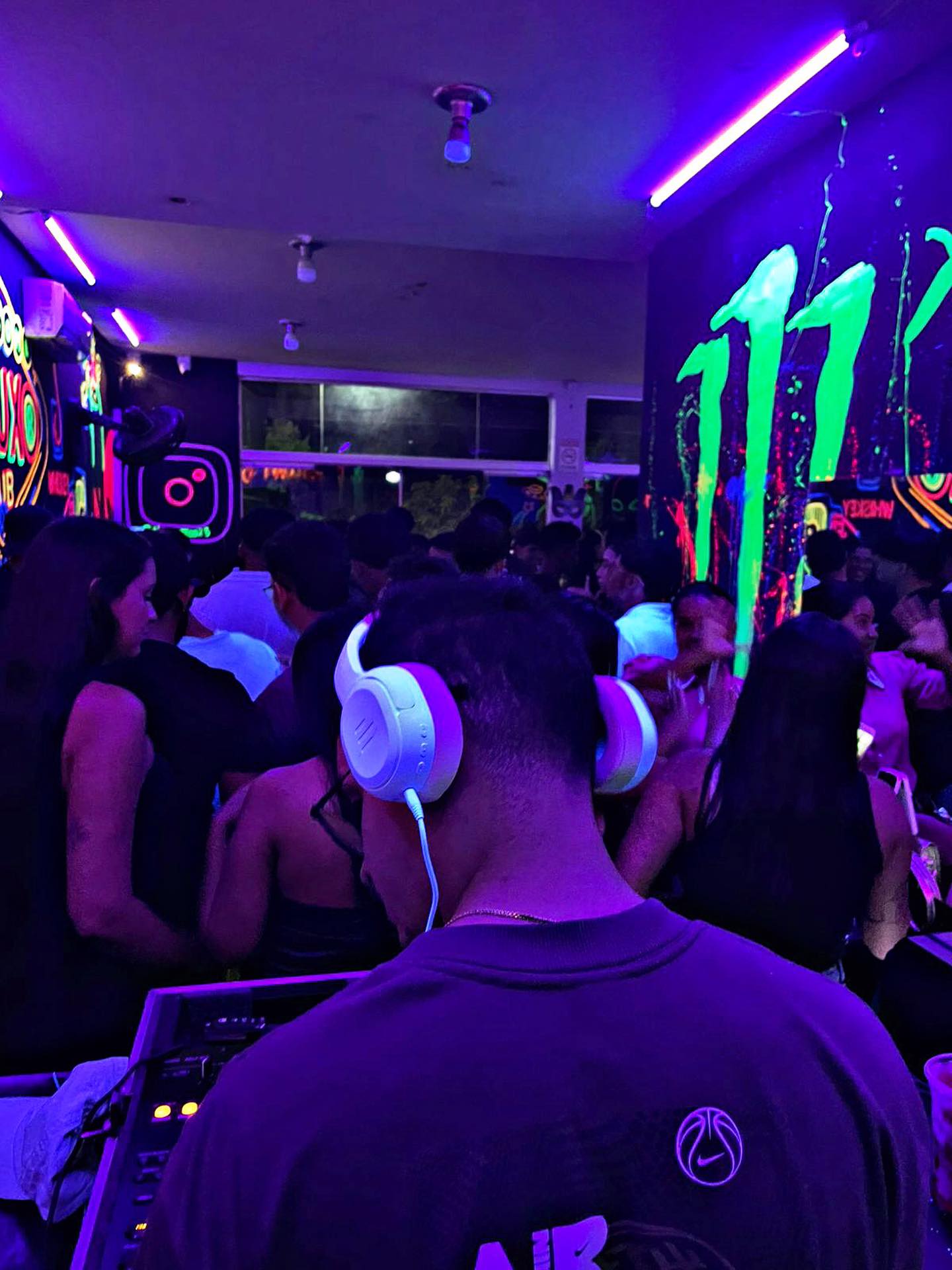 DJ Gugu de costas na cabine com o público sob iluminação violeta
